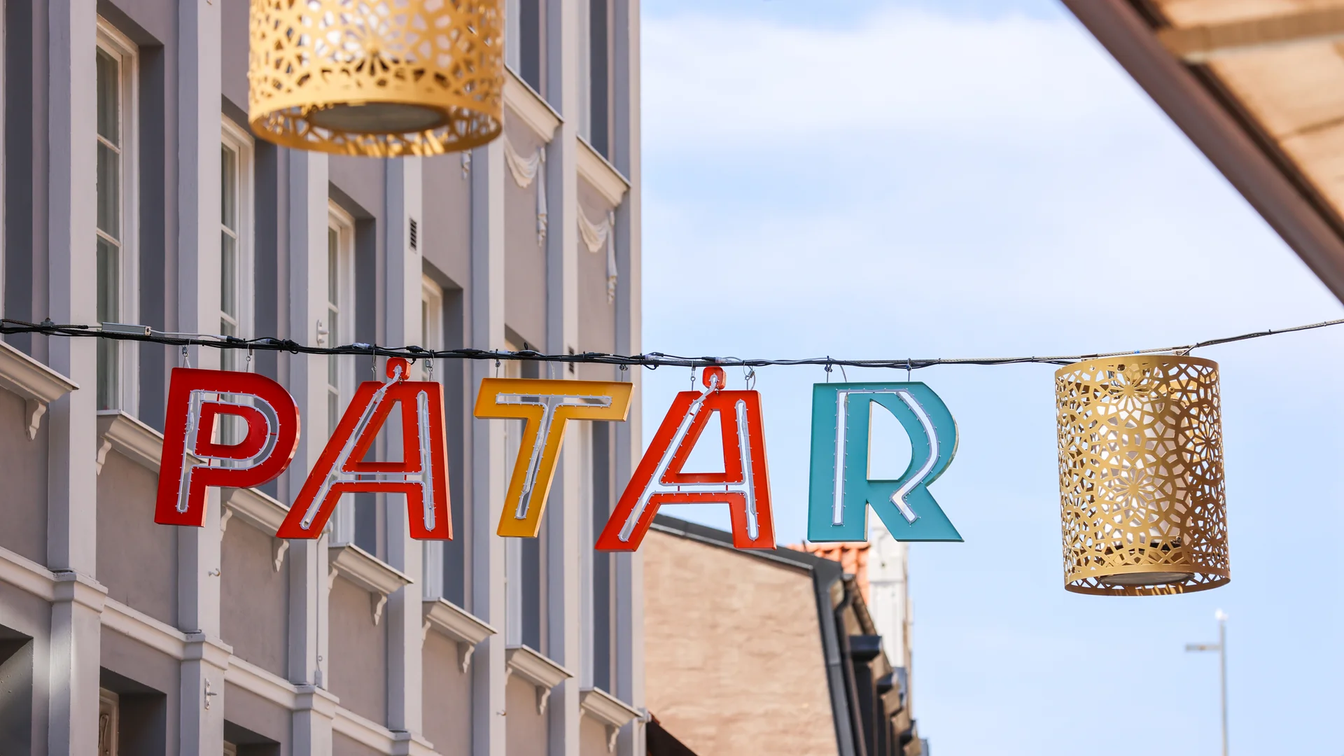Närbild på färgglada bokstäver över gata som bildar ordet "påtår"